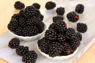 Sweet blackberry in bowls on wooden table