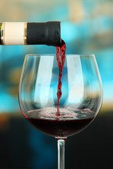 Red wine being poured into wine glass, on bright background