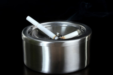 Metal  ashtray with cigarette, isolated on black