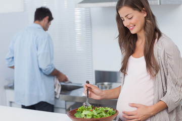 Obraz na płótnie Canvas Pregnant woman mixing a salad in the kitchen