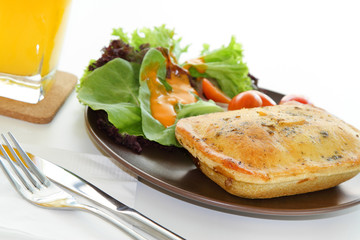A meal of chicken pie with salad and a glass of orange juice