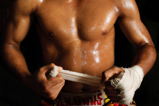 The muscular fighter tying tape around his hand preparing to