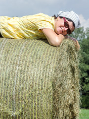 Naklejka na ściany i meble Peasant woman is lying on the hay bales