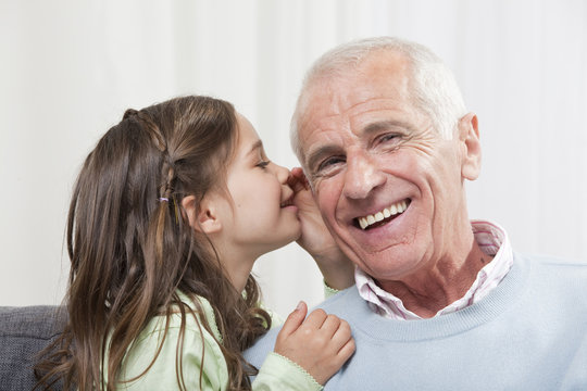 Girl whispering into grandfather's ear, close-up