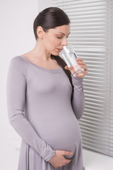 Pregnant woman drinking water. Mature pregnant woman standing ne