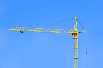 Yellow construction tower crane against blue sky