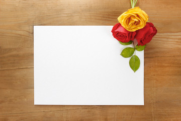 Red and yellow roses on wooden background. Blank sheet of paper,