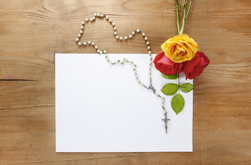 Colorful roses and white rosary on wooden background. Blank shee