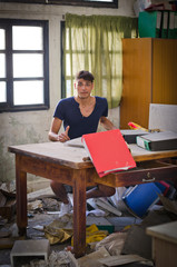 Young man in very messy office looking puzzled