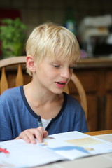 Cute schoolboy is studiyng at home reading a book