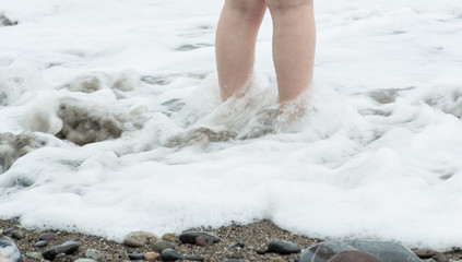 Legs of a little girl in foamy sea water