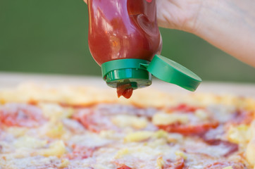 Human hand holding ketchup bottle above pizza
