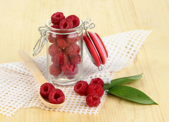 Ripe raspberries in bank on wooden table close-up