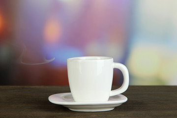 Cup of coffee on wooden table on bright background