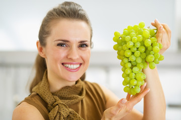 Portrait of smiling young housewife showing branch of grapes