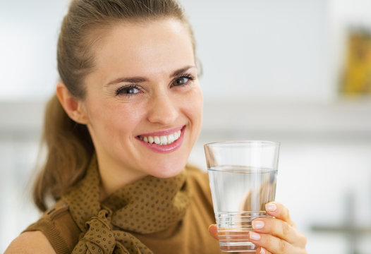 Portrait of happy young woman drinking water in kitchen