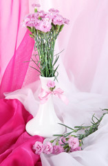 Many small pink cloves in vase on light fabric background