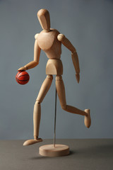 Wooden mannequin with basketball ball on grey background