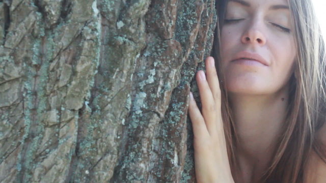 Happy beautiful girl hugging big tree in park