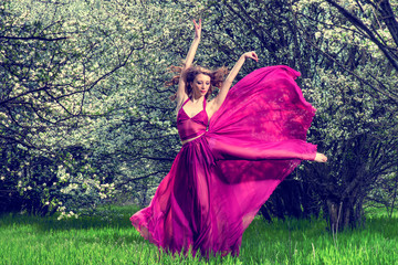 Woman in airy crimson dress dancing among the blossoming trees