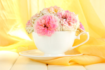 Roses in cup on wooden table on yellow cloth background