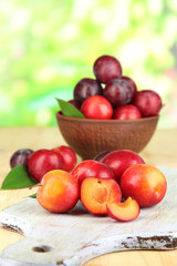 Fototapeta na wymiar Ripe plums in bowl on wooden table on natural background