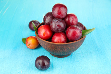 Ripe plums in bowl on wooden table close-up
