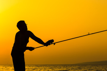 Fisherman's silhouette on the beach at colorful sunset