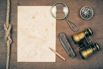 Compass, binoculars, paper, pencil, magnifying glass on wood