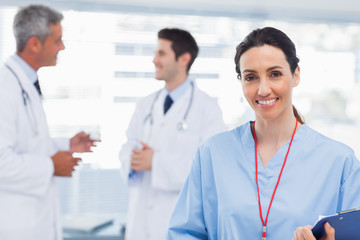 Nurse smiling at camera while doctors are talking together