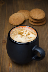 black coffee with foam and oatmeal cookies in the background