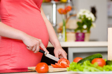 Obraz na płótnie Canvas Close up pregnant woman with knife on kitchen cuts tomato
