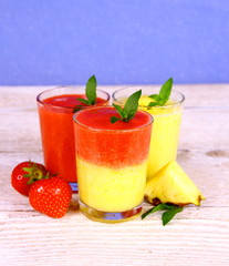 Strawberry and pineapple smoothie in glass on blue background