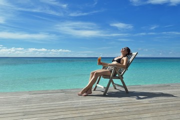 Beautiful young woman with a drink by the sea