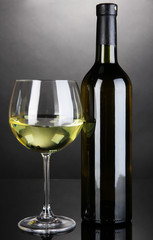 White wine glass and bottle of wine on grey background