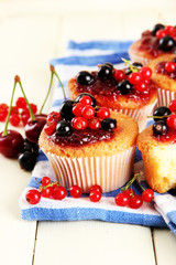 Tasty muffins with berries on white wooden table