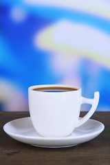 Cup of coffee on wooden table on bright background