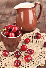 Ripe red cherry berries in cup on wooden table close-up