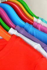 Different shirts on colorful hangers on grey background