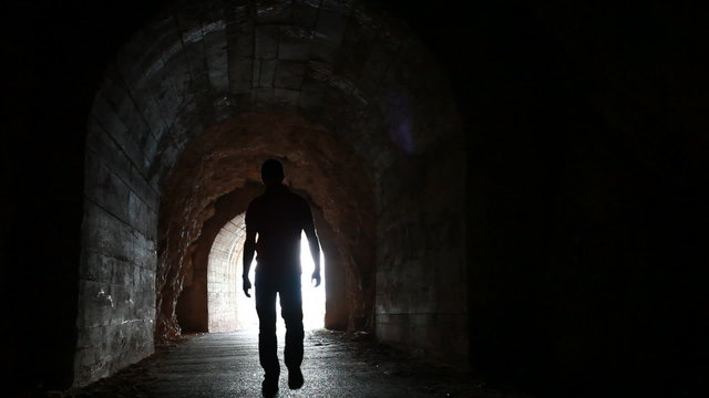 Man goes through the dark concrete tunnel into the glowing end