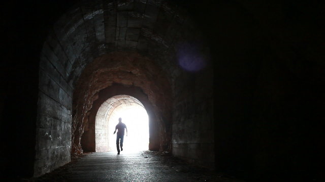 Man runs into the dark concrete tunnel from the glowing end