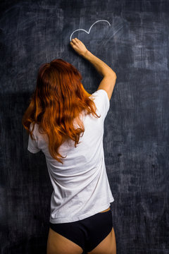 Redhead woman in underwear drawing on a blackboard