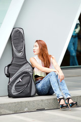 Fototapeta premium Young beautiful woman posing outdoor with her guitar gig bag
