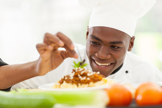 Afro American chef in restaurant kitchen garnishing pasta dish