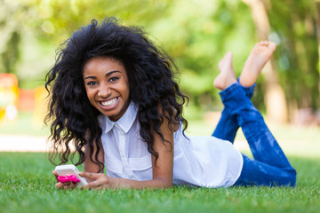 Teenage black girl using a phone, lying on the grass - African p