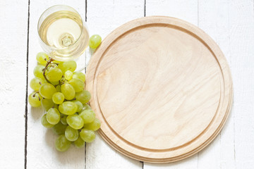 Glass of wine and grapes with empty cutting board background