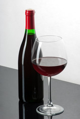 Wine bottle and a glass filled with wine on a black reflective s