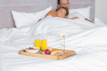 Obraz na płótnie Canvas Cuddling couple asleep with breakfast tray on bed