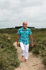 Retired senior man with beard and glasses walking outdoors in gr