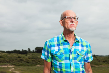 Naklejka na ściany i meble Retired senior man with beard and glasses outdoors in grass dune